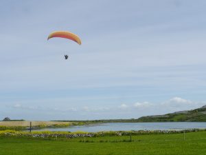 Yellow paraglider flying over blue lake (Lough Murree) and green fields