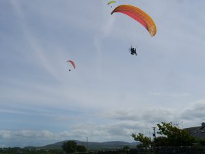 Three orange and yellow paragliders Flying over grey Burren Mountains