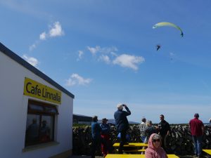 Yellow paraglider flying over Cafe Linnalla. People watching him.